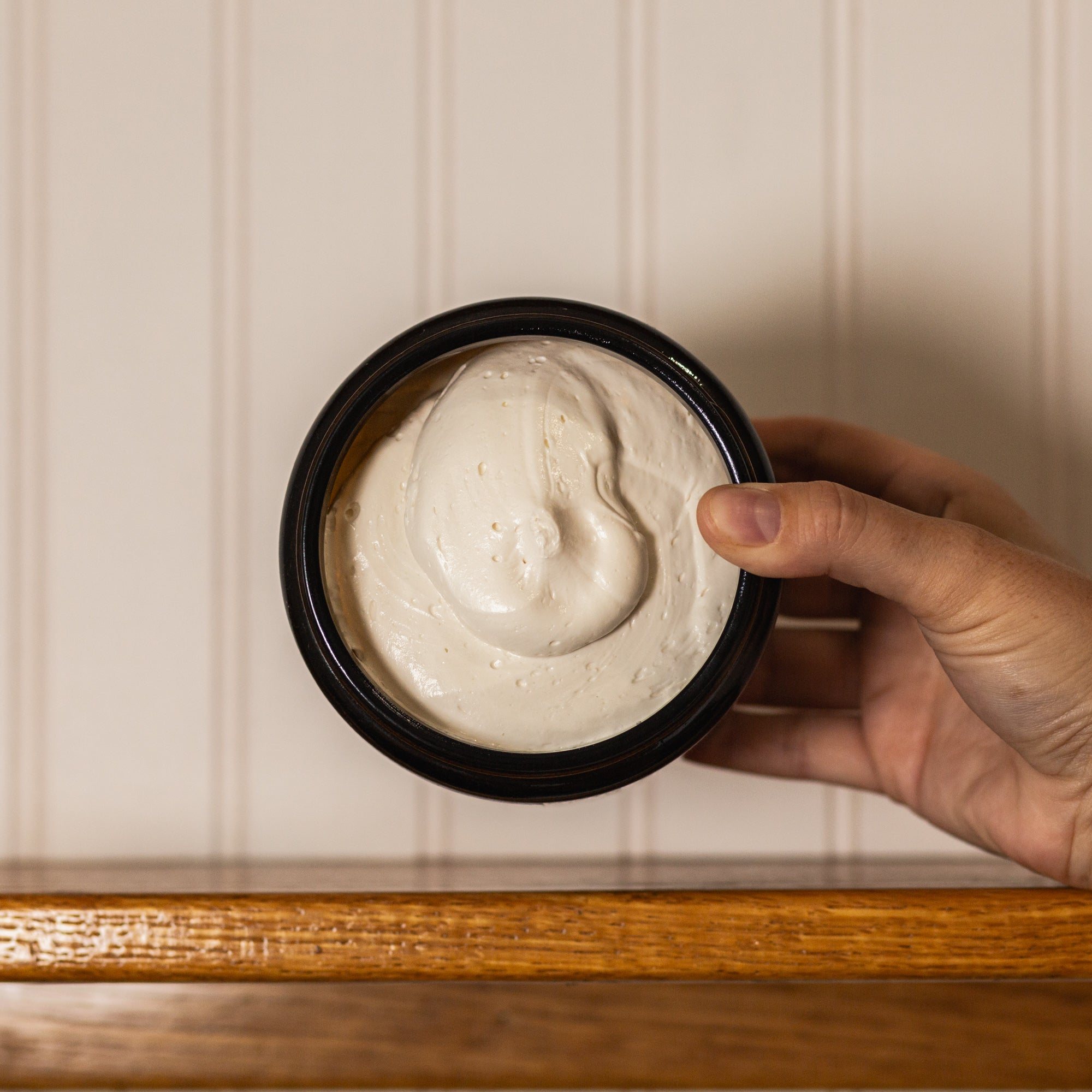 Hand holding an open jar of HydroTallow body whip